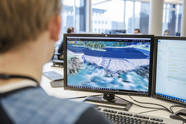 Mann foran to skjermer, en skjerm viser modeller av en demning