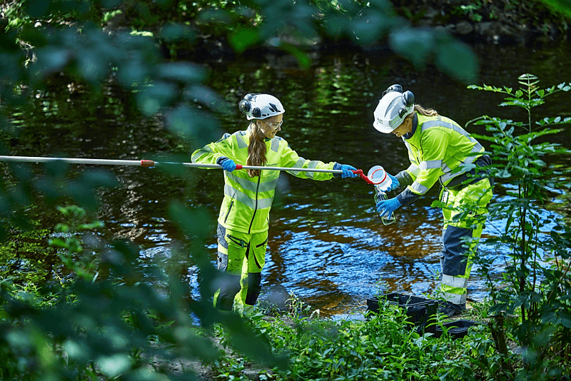 To personer i vernelklær tar vannprøver i elv
